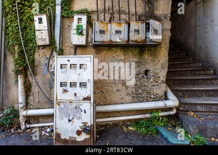Several generations of electricity meter boxes on a moss-covered house wall in Chugureti, Tbilisi, Georgia. The ornate staircase on the right, with its decorative ceramic tiles, bears witness to the building’s former grandeur; ivy grows through the cracks in the weathered façade – a symbol of the backlog of renovation work in Tbilisi’s old neighbourhoods. Kumisi Street, Chughureti, Kveda Chugureti, Chugureti District, Tbilisi, 0102, Georgia Stock Photo