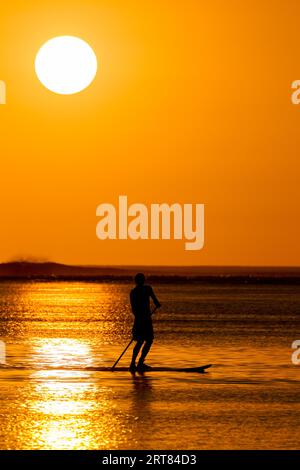 Stand up paddlers in front of the sunset in Le Morne, Mauritius Stock Photo
