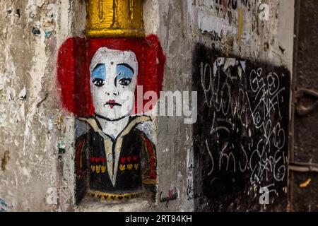Mural on Kote Abkhazi Street in Tbilisi’s Old Town, Georgia: a figure with red hair, a golden crown and heart motifs on her clothing is reminiscent of the Queen of Hearts from Lewis Carroll’s *Alice’s Adventures in Wonderland*. The painting is situated on a weathered plaster wall alongside graffiti and peeling posters. Kote Abkhazi Street, Kala, Ortachala, Krtsanisi District, Tbilisi, 0108, Georgia Stock Photo
