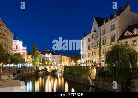 The promenade on the Ljubljanica river in the slovenian capital city Ljubljana with the Triple bridge and famous pink franciscan church at night Stock Photo