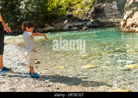 A boy playing and throwing stones in the turquoise river of the Valbona valley, Theth national park, Albanian Alps, Albania Stock Photo