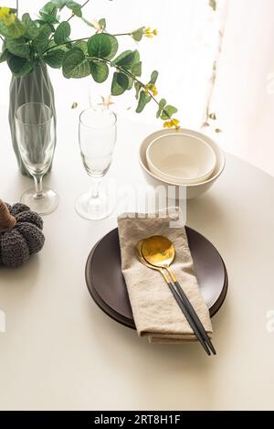 Dinner table setting with white and brown ceramic plates, golden cutlery set and  eucalyptus leaves in vase on white table top view. Plate mockup. Stock Photo