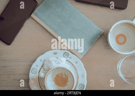 Two empty coffee cups, book and mobile phones on wooden table. Breakfast table. Morning drinks. Cafe interior. Urban lifestyle. Coffee break. Stock Photo