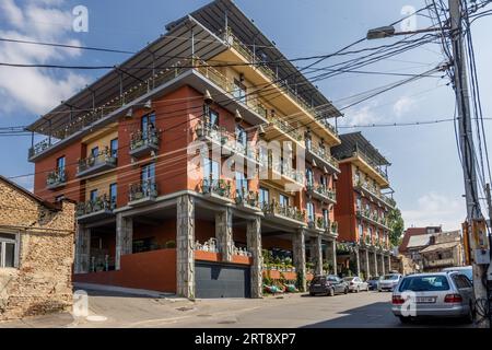 A residential building with planted balconies and large bells hanging beneath the balcony slabs stands in the Chugureti district of Tbilisi, Georgia. Flower pots line the balcony railings. A metal roof on posts spans the top terrace. A tangle of power and telephone cables hangs in front of the building. Stock Photo
