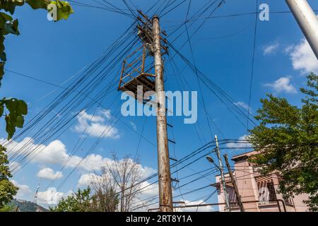 An electricity pylon with a work platform and a branching bundle of cables in the Chugureti district of Tbilisi. Residential buildings and the wooded Mtatsminda Hill can be seen in the background; the power networks in the older neighbourhoods date largely from the Soviet era and have not undergone any major refurbishment since then. Chugureti, Tbilisi, Georgia, Europe Stock Photo