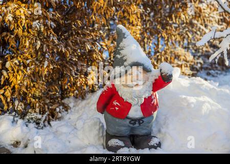 Beautiful view of smiling figure of gnome Santa Claus standing in snow in winter garden. Sweden. Stock Photo