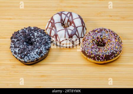 Close-up view of three colorful donuts sprinkled with icing and chocolate, isolated on wooden background. Food and drink concept. Stock Photo