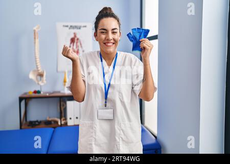 Young hispanic woman holding hand support screaming proud, celebrating victory and success very excited with raised arm Stock Photo