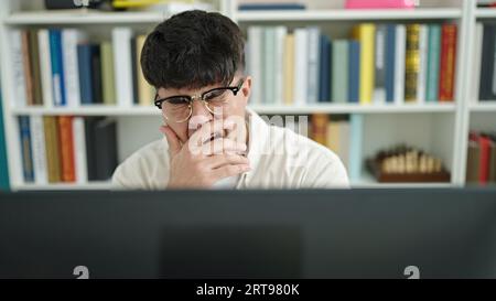 Young hispanic man student tired using computer yawning at library university Stock Photo