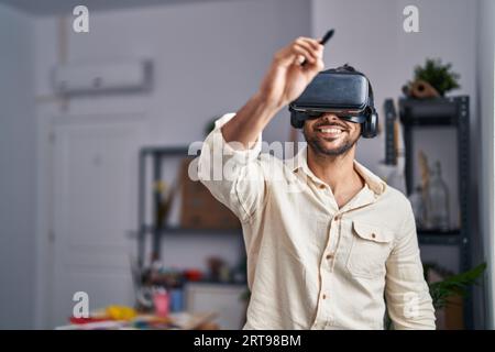 Young hispanic man artist using virtual reality glasses drawing at art studio Stock Photo