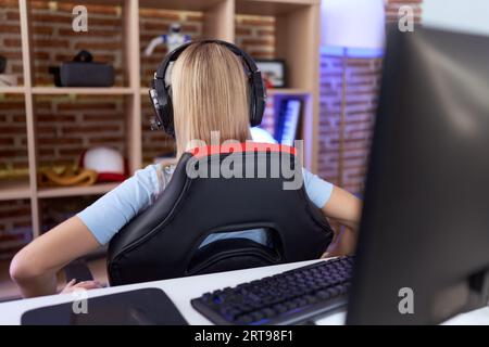 Young caucasian woman playing video games wearing headphones standing backwards looking away with arms on body Stock Photo