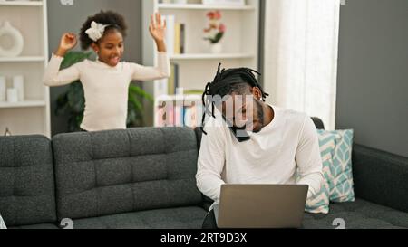African american father and daughter sitting on sofa working while child disturb at home Stock Photo