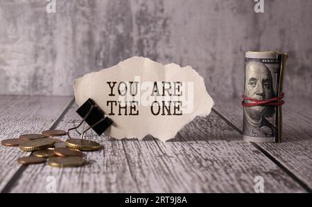 A man is holding a piece of paper which is saying 'You are the one '. The paper is white with black handwritten letters and the background is red. Stock Photo