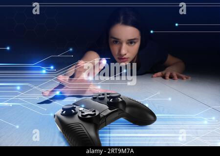 Gaming disorder. Woman reaching out for gamepad on floor from darkness. Circuit board pattern Stock Photo