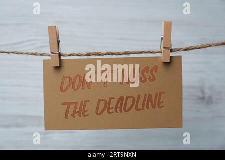 Note with reminder Don't Miss The Deadline hanging on twine against light background Stock Photo