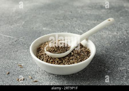 Bowl of caraway (Persian cumin) seeds and spoon on gray textured table Stock Photo