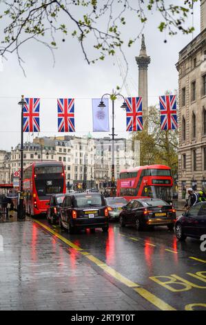 LONDON - April 24, 2023: A quintessential London scene: classic black taxi cabs, red double-decker buses, Union Jack flags, and the historic backdrop Stock Photo