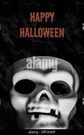 Happy Halloween sign or invitation with skull on black background with smoke. Halloween sign written in orange letters. Copy space Stock Photo