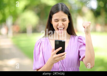Front view portrait of an excited woman checking cell phone content outdoor Stock Photo