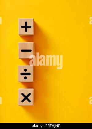 Basic mathematical operations symbols. Plus, minus, multiply and divide symbols on wooden cubes on yellow background. Mathematic or math education and Stock Photo