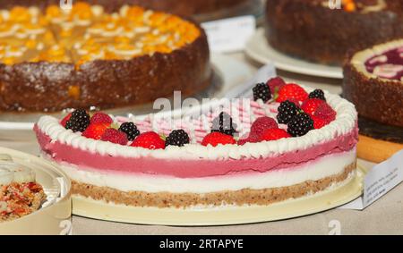 Pastry stand with variations of no-bake RAW cakes, no-bake raw fruit cake with coconut cream in the foreground, embellished with fresh strawberries, r Stock Photo