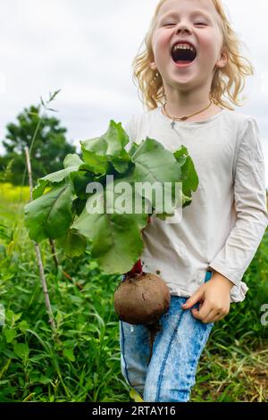 Adorable girl on the farm, smiling while holding a bunch of homegrown beets Stock Photo