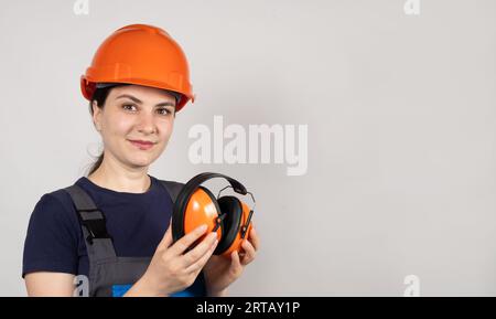 Female construction worker in protective helmet holding earmuffs on white background. Stock Photo