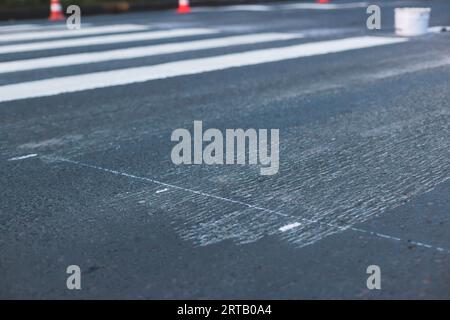 Process of making new road surface markings with a line striping machine, workers improve city infrastructure, demarcation marking of pedestrian cross Stock Photo