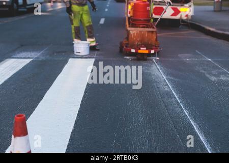 Process of making new road surface markings with a line striping machine, workers improve city infrastructure, demarcation marking of pedestrian cross Stock Photo