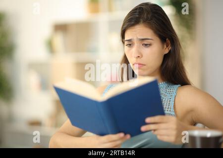 Sad woman reading a paper book sitting at home Stock Photo