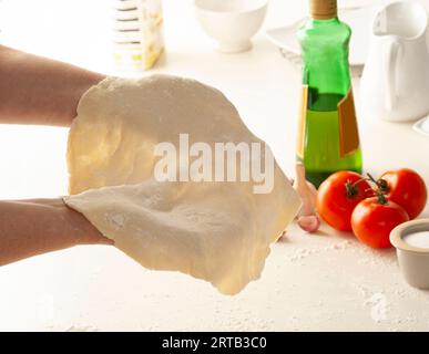 Woman preparing pizza dough by rolling it with her hands. The process of making pizza. Focus on a woman's hands. Stock Photo
