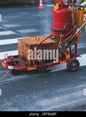 Process of making new road surface markings with a line striping machine, workers improve city infrastructure, demarcation marking of pedestrian cross Stock Photo