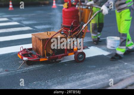 Process of making new road surface markings with a line striping machine, workers improve city infrastructure, demarcation marking of pedestrian cross Stock Photo