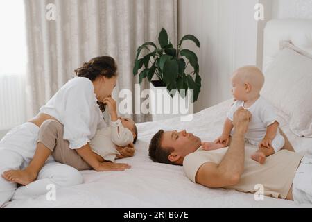 Family with two kids on the bed having fun. Mather, father baby and toddler sons are happy in the morning in bedroom. Children playing with parents at Stock Photo