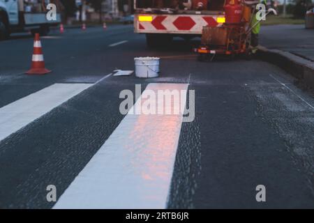 Process of making new road surface markings with a line striping machine, workers improve city infrastructure, demarcation marking of pedestrian cross Stock Photo