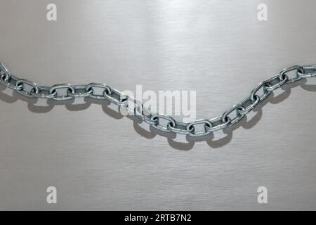 Top view of handmade customized reflecting link metal chain with shadow placed in zigzag shape on silver background in glowing light Stock Photo
