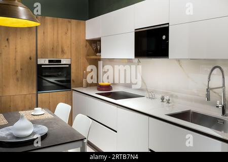 Interior of modern kitchen under renovation with white cabinets platform washbasin water tap stove with appliances oven and dining zone with table cha Stock Photo