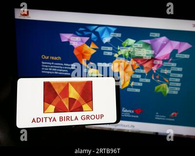 Person holding smartphone with logo of Indian company Aditya Birla Group (ABG) on screen in front of website. Focus on phone display. Stock Photo