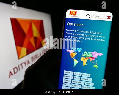 Person holding smartphone with webpage of Indian company Aditya Birla Group (ABG) on screen in front of logo. Focus on center of phone display. Stock Photo