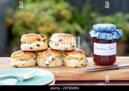 A freshly baked batch of fruit scones displayed on a serving board with a jar of homemade Damson Jam. All served to an outdoor table Stock Photo