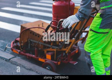 Process of making new road surface markings with a line striping machine, workers improve city infrastructure, demarcation marking of pedestrian cross Stock Photo