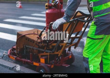 Process of making new road surface markings with a line striping machine, workers improve city infrastructure, demarcation marking of pedestrian cross Stock Photo