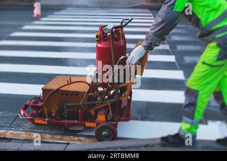 Process of making new road surface markings with a line striping machine, workers improve city infrastructure, demarcation marking of pedestrian cross Stock Photo