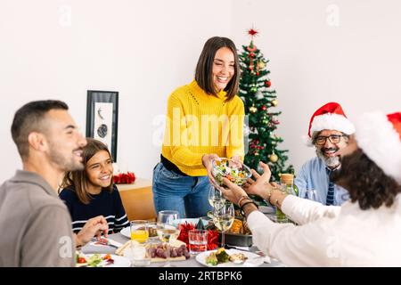 Happy young woman serving salad at dining table during christmas celebration Stock Photo