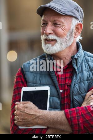 Portrait of senior caucasian man with white beard and hair holding tablet on farm Stock Photo