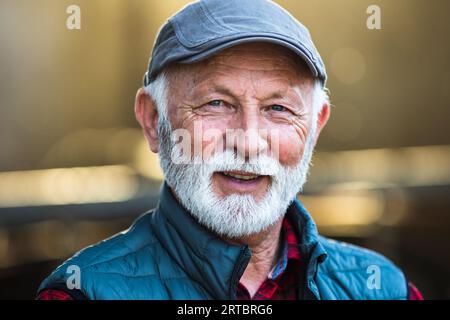 Portrait of senior caucasian man with white beard and hair wearing cap on farm Stock Photo