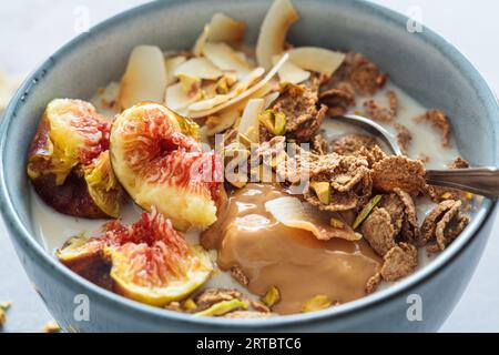 Multigrain wholewheat breakfast cereals with fig, coconut chips, peanut butter and pistachio, close-up. Vegan breakfast concept. Stock Photo