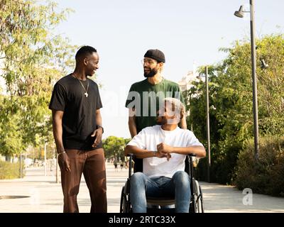 Group of young diverse male friends walking through a city, one of them in a wheelchair. Friendship and disability Stock Photo