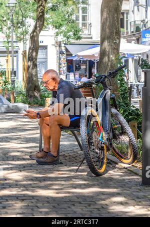 Older man with cross bike sitting on city center bench studying smartphone - Tours, Indre-et-Loire (37), France. Stock Photo