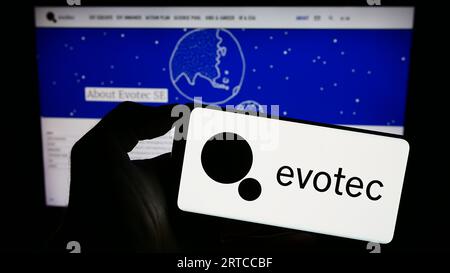 Person holding smartphone with logo of German drug discovery company Evotec SE on screen in front of website. Focus on phone display. Stock Photo